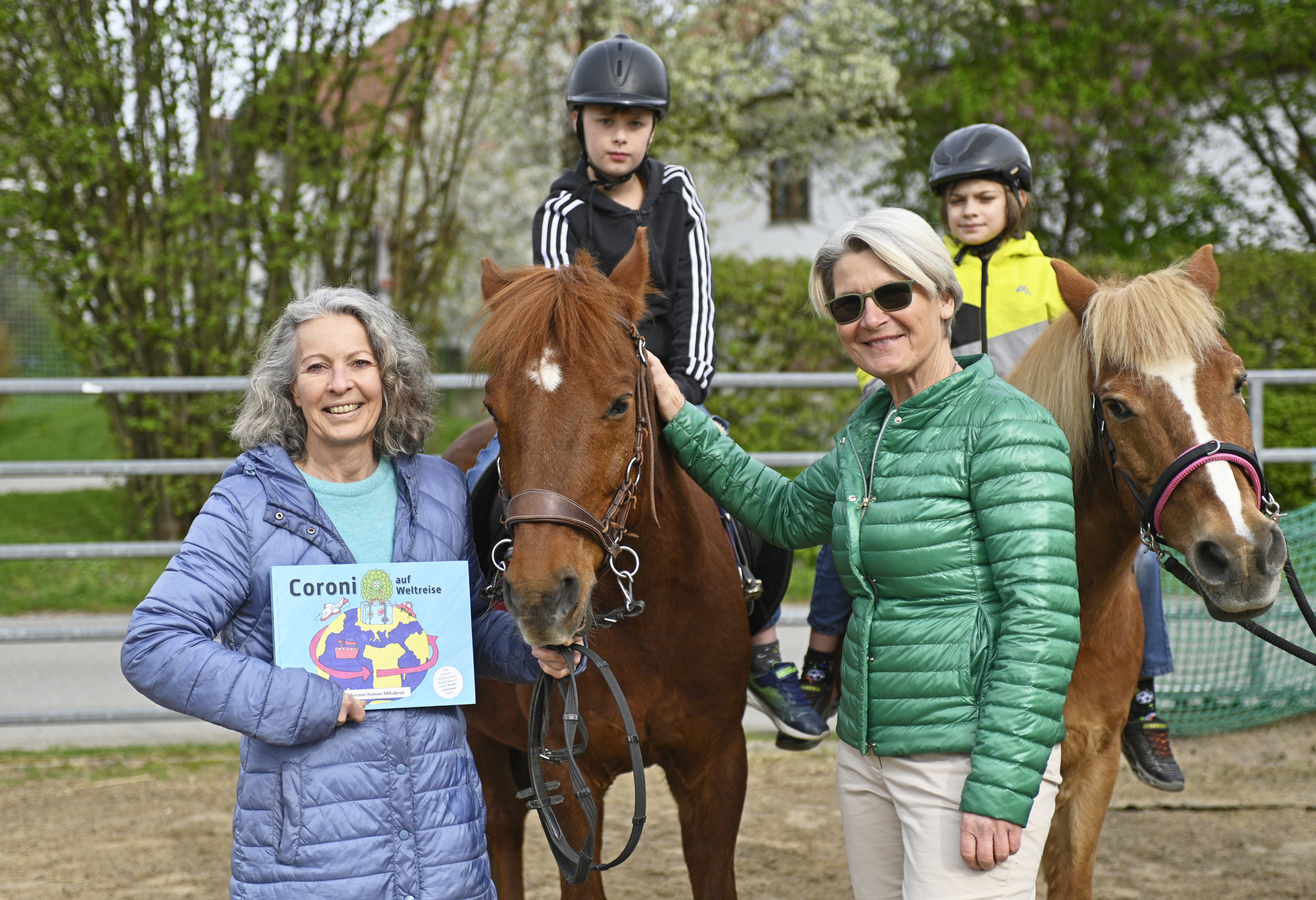 Susann Mihaljevic mit ihrem Kinderbuch "Coroni auf Weltreise", einer Betreuerin und Kinder auf Therapiepferden