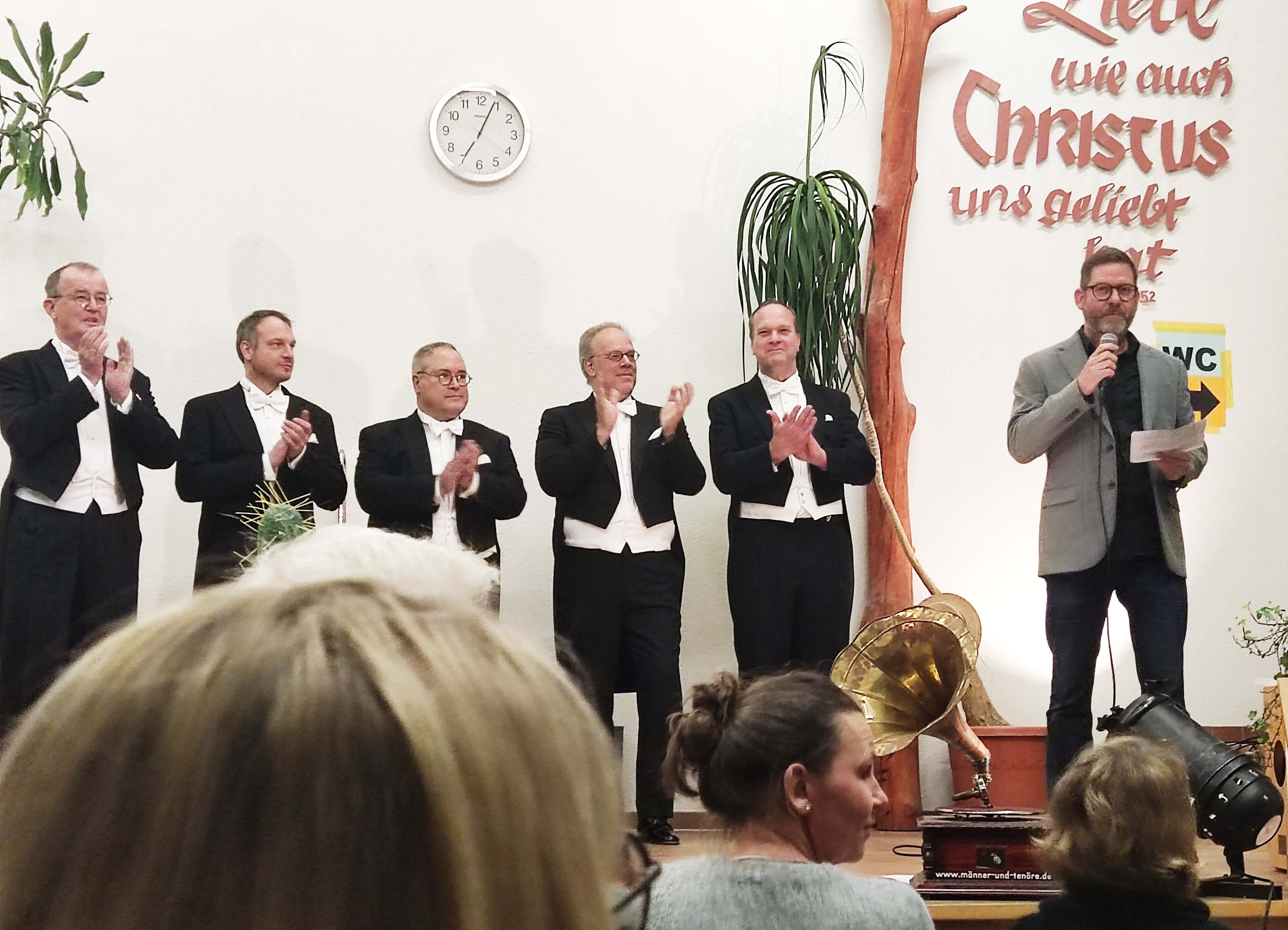 Mehrere Sänger und ein Moderator stehen auf der Bühne vor Publikum.